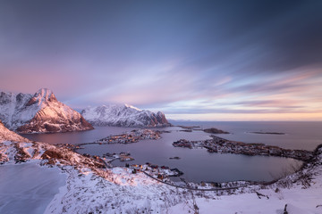Fantastic purple sunrise seen from Reinebringen summit. View on Reinevatnet lake, Reine village and fjord during snowy winter. Lofoten, Norway