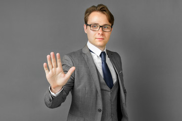 Portrait of a businessman in a suit who stretches out his hand in front of his palm. Stop. Gray background.