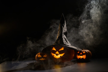 Three jack o lanterns glow in the dark amidst the fog. Halloween pumpkin in a witch hat.