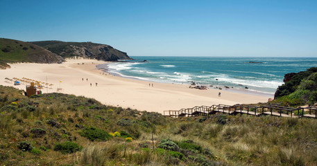 Fototapeta na wymiar Wild beach on seaside of Portugal. Sunny sand area and ocean waves at nice day