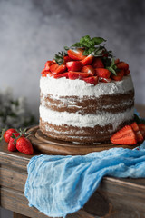 Naked cake with cream, decorated with strawberry and mint. Chocolate cake.