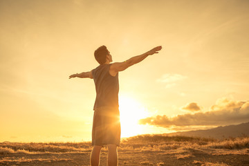 Fototapeta na wymiar Strong young man with arms outstretched feeling at peace and inspired by the beautiful nature sunrise.