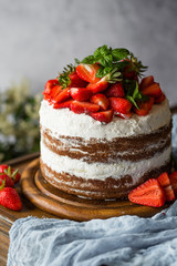 Naked cake with cream, decorated with strawberry and mint. Chocolate cake.
