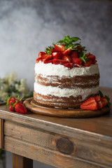 Naked cake with cream, decorated with strawberry and mint. Chocolate cake.