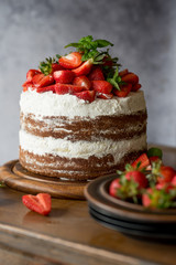 Naked cake with cream, decorated with strawberry and mint. Chocolate cake.