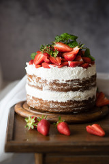 Naked cake with cream, decorated with strawberry and mint. Chocolate cake.