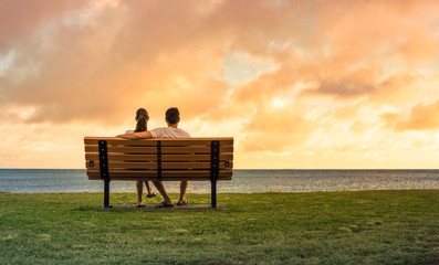 couple sitting on park bench watching the sunset. Love and relationships concept.  - obrazy, fototapety, plakaty
