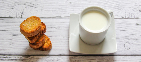 Cup of warm milk and bread crumbs on a wooden background. White Cup with milk.