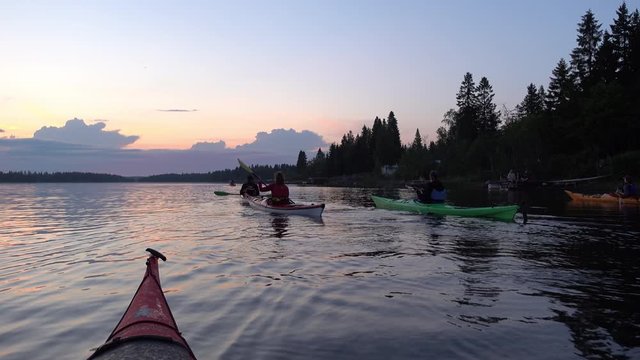 Group of young people kayaking during light night in Swedish Lapland, calm water, summer forest. Healthy activity, midnight, low Sun behind clouds