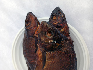 Smoked bream on a white plastic plate. Golden smoked fish close up top view. Hot smoked fish. Food photo. 