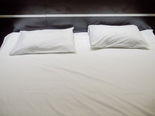 Two rectangular pillows in white pillowcases lie on a white sheet