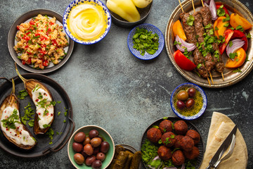 Middle eastern or Mediterranean dinner with grilled kebab, falafel, roasted and fresh vegetables, assorted Arabic meze and appetizers on rustic background table. Dinner table overhead, space for text
