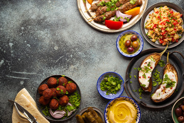 Middle eastern or Mediterranean dinner with grilled kebab, falafel, roasted and fresh vegetables, assorted Arabic meze and appetizers on rustic background table. Dinner table overhead, space for text
