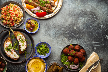 Fototapeta na wymiar Middle eastern or Mediterranean dinner with grilled kebab, falafel, roasted and fresh vegetables, assorted Arabic meze and appetizers on rustic background table. Dinner table overhead, space for text 