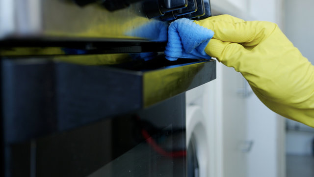 Closeup Image with Person Hands Wearing Protective Yellow Household Gloves in the Kitchen and Cleaning a Stove