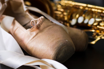 close up on pointe shoes, defocused saxophone background, short depth of field.