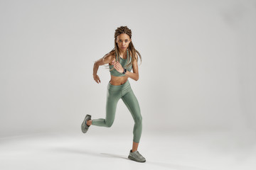 Never stop. Full length shot of young sportive mixed race woman in sportswear looking at camera while running or exercising isolated over grey background