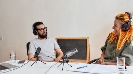 Two bloggers, young man and woman in headphones looking at each other while talking, recording...