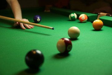 pool balls and billiard cue on green billiard table. the hand of a billiard player holds a cue on a pool table. billiard player strikes a white ball