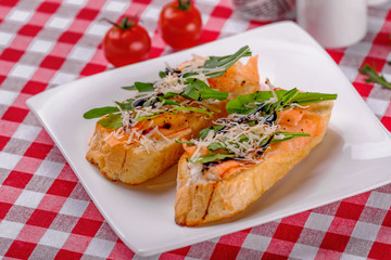 Italian Appetizer Bruschetta with Salmon, parmesan, balsamic vinegar and fresh arugula on white plate in italian restaurant background, top view. Italy food. Close up.