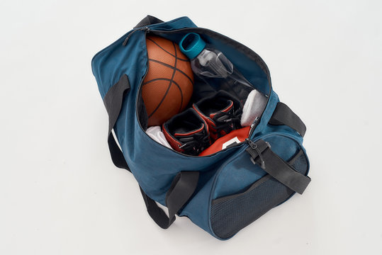 Basketball player outfit. Top view of a sports bag with professional uniform, ball, sneakers and bottle of water isolated on grey background