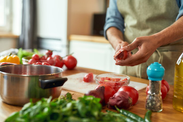 Close up of man cook holding knife, cutting tomatoes while preparing healthy meal with vegetables in the kitchen. Italian cuisine concept