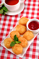 Doughnuts. Freshly made donuts from cottage cheese with berry jam and black tea on breakfast. Balls from the cottage cheese, the dessert on white plate in restaurant background, top view.