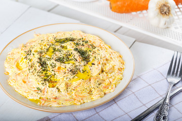 Fresh carrot salad with garlic yogurt in dish on wooden background.