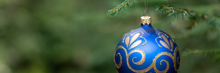 blue with gold patterns ball decorate the green branches of the Christmas tree.