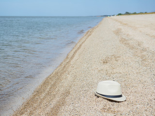 Fototapeta na wymiar A white straw hat lies on the sand by the water. Sea beach on a summer sunny day. Sea vacation concept. Copy space. High quality photo