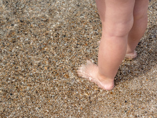 Small baby feet close-up on the sand of the sea beach. Sea water washes the feet. Happy childhood. Rest at the sea. Summer sunny day. Copy space.