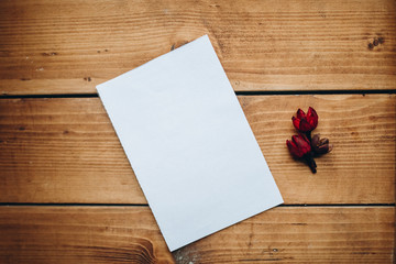 Blank white paper with dry flower on a wooden desk.
