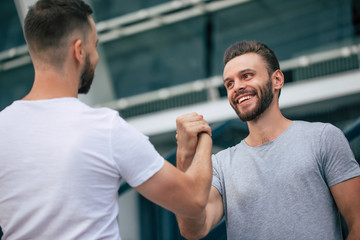 Men's friendly handshake. Two young bearded handsome friends in casual t-shirts are posing together...