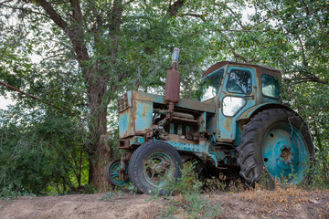 Obraz premium Vintage photo - an old blue tractor standing under a green branching tree