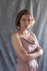 portrait of young caucasian woman with short hair posing in pink suit, standing in front of fabric background. model tests of pretty girl in blouse. attractive pensive female poses with arms crossed