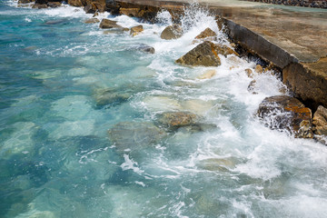Wonderful views of the blue Mediterranean Sea. Sunny rocks, waves with foam and splashing water. The wave crashes into the rocks on the shore