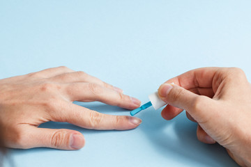 woman at a nail care procedure. a manicurist paints a girl's nails on her hand with blue nail polish