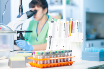 Female professional in uniform. Work with a light microscope in a research laboratory, testing laboratory. Histology, histopathology, microscopic analysis of patients, biopsy with cancer, Covid-19.
