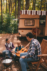 Happy family on a camping trip relaxing in the autumn forest. Camper trailer. Fall season outdoors trip