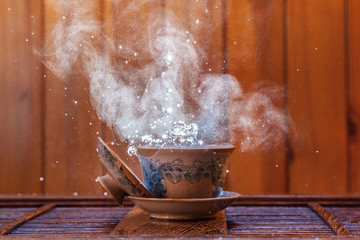 Traditional chinese painted clay tea brewing cup with cloud of steam and splashing hot water on...