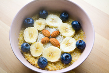 Bowl of breakfast oatmeal with bananas, blueberries, coconut and almonds in a pink bowl