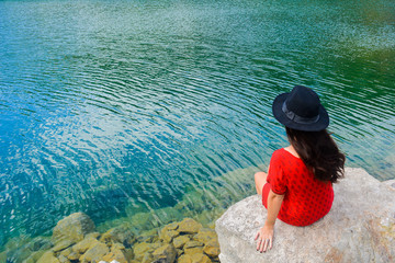 Young brunette woman sitting on a rock by a beautiful blue lake
