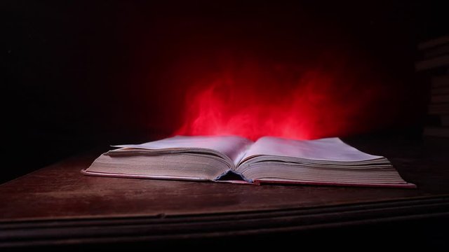 A stack of old books. Vintage book on wooden table. Magic lightning around a glowing book in the room of darkness. Selective focus