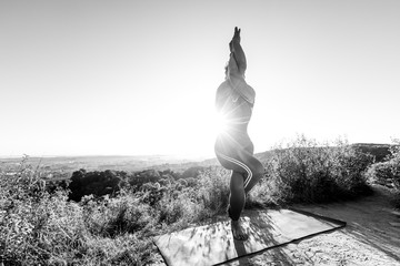 Black and White photo The rays of the sunrise shine yoga master standing on a hill in a yoga pose Eagle Pose Garudasana