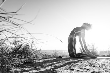 Obraz na płótnie Canvas Black and White photo how woman looks at the sky and does sports yoga in the position of a camel at sunrise