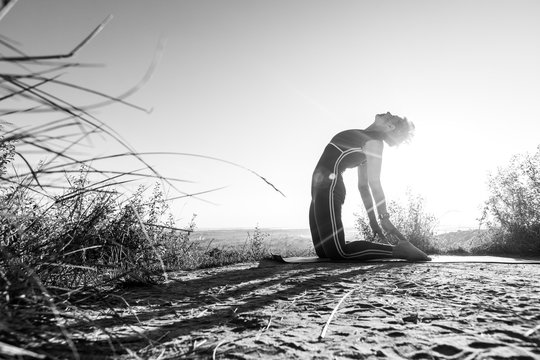 Black and White photo a woman who does sports yoga in the position of a camel at sunrise