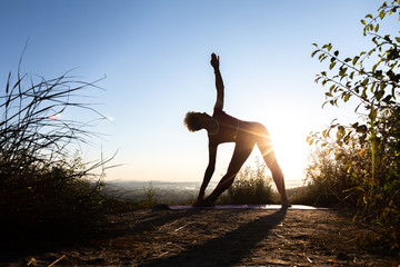Woman master of zen yoga in dark doing exercises at sunrise in triangle pose