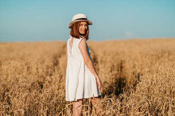 young girl happily walks in slow motion through a yellow field, touching the ears of wheat with her...