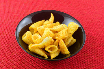 Pizza flavored cone shaped corn snacks in black bowl on red tablecloth