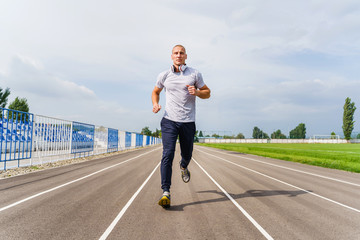 Full length front view on adult caucasian man jogging on the running track - Blonde male athlete in...
